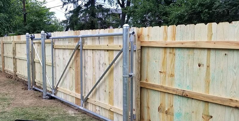 Wooden fence with a metal gate in a yard.