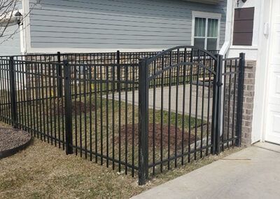 Black metal fence enclosing a small yard area next to a house with gray siding.