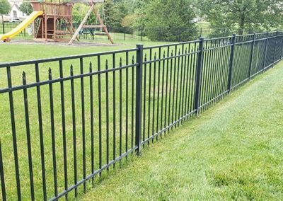 Black metal fence encloses a grassy backyard with a play structure.