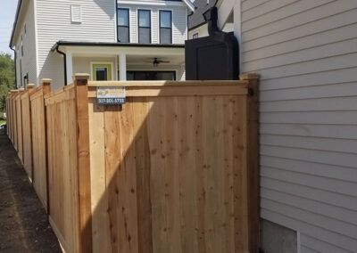 Wooden fence next to a house with a dark container on top.