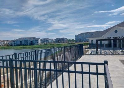 Lakeside apartment buildings under a bright blue sky with a black iron fence in the foreground.