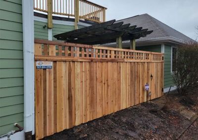 Wooden fence with lattice top along a green house, with a dark pergola visible behind the fence.
