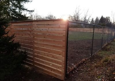 Wooden and chain-link fence, the sun is shining behind it.