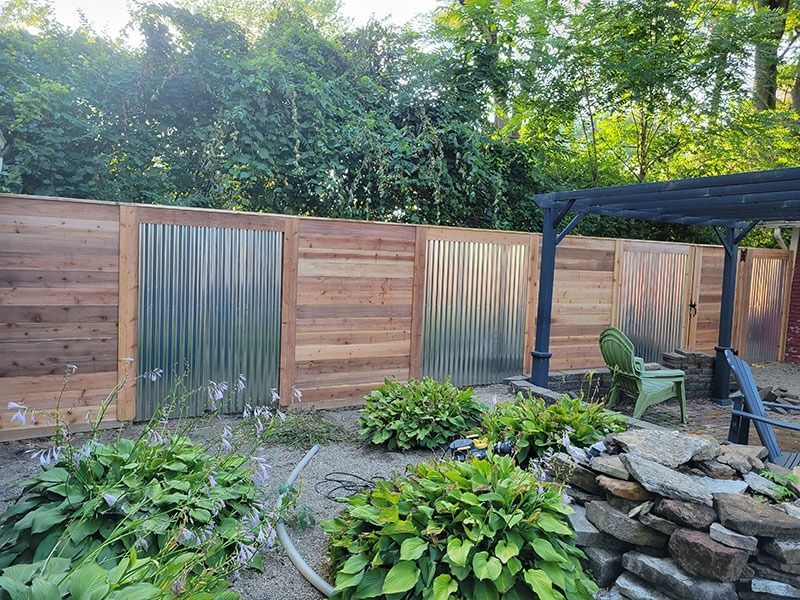 Wooden and corrugated metal fence in a backyard garden, featuring green foliage, and a dark pergola.