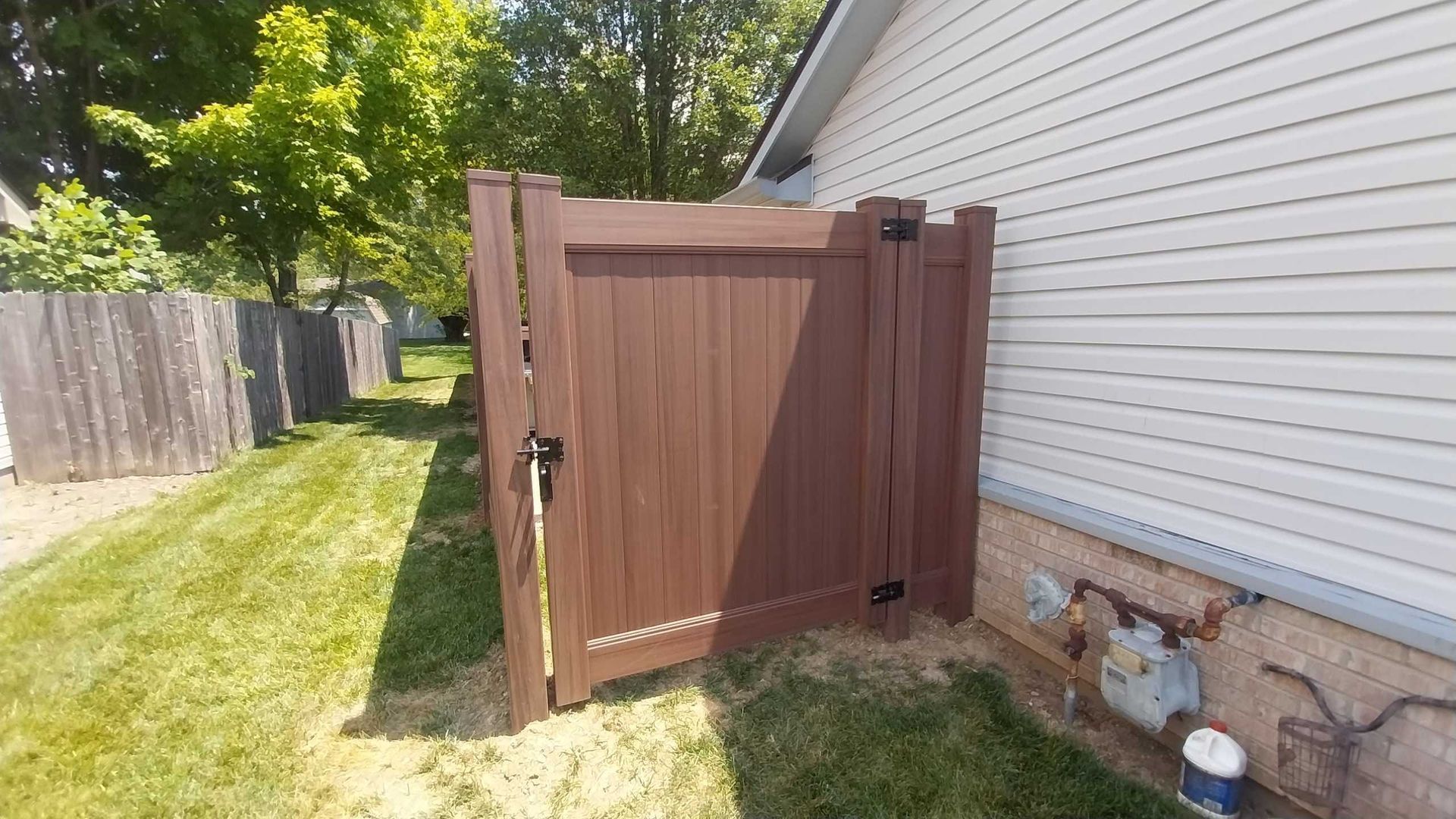 Brown gate in a yard, attached to a house with siding, next to a gas meter.