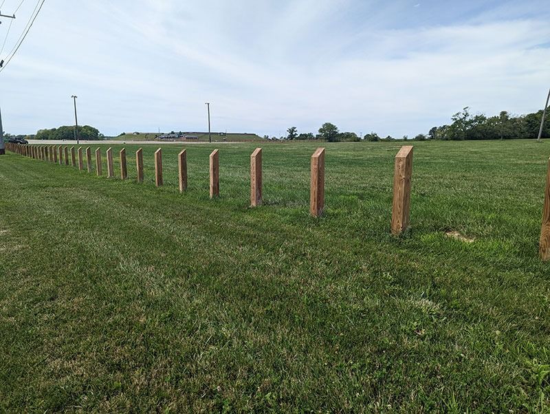 Wooden fence posts in a grassy field on a sunny day.