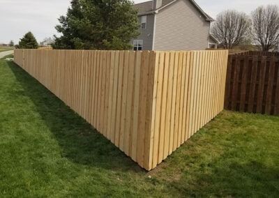 Wooden fence surrounding a grassy yard next to a brown, slatted fence.