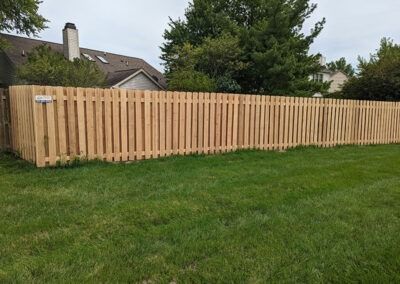 Wooden picket fence in a grassy yard, with houses in the background.