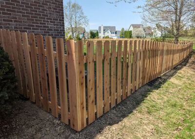 Wooden picket fence surrounds a yard on a sunny day.