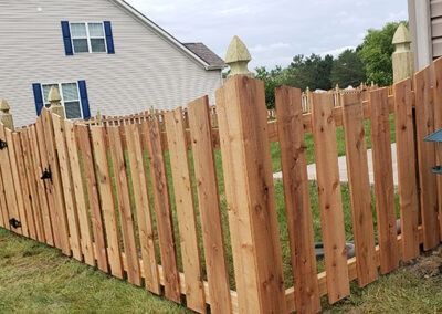 Wooden picket fence with decorative posts in a residential yard.