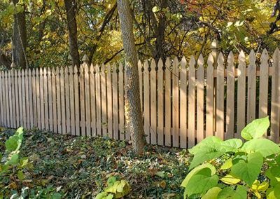 Wooden picket fence in front of fall foliage.