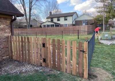 Wooden gate and fence in a backyard, person working, residential setting.