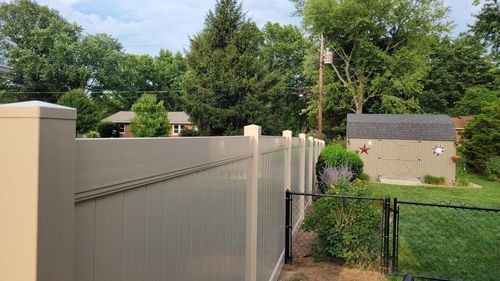 Tan vinyl fence bordering a backyard with a shed, trees, and partial house visible.