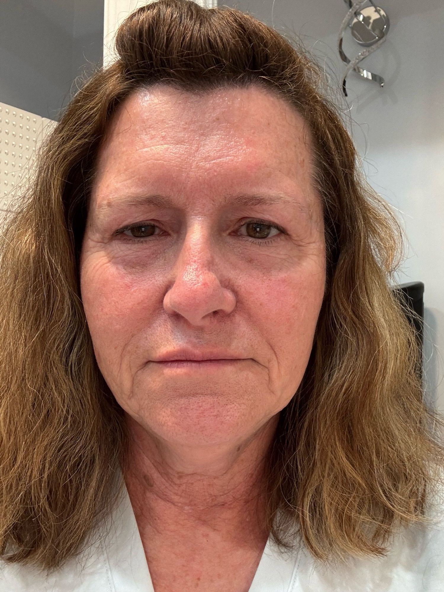 Close-up portrait of a woman with wavy brown hair and a neutral expression indoors