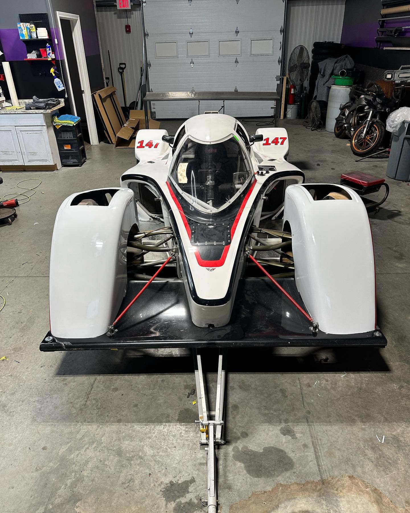 White race car with red accents in a garage setting. Number 147 on the side.
