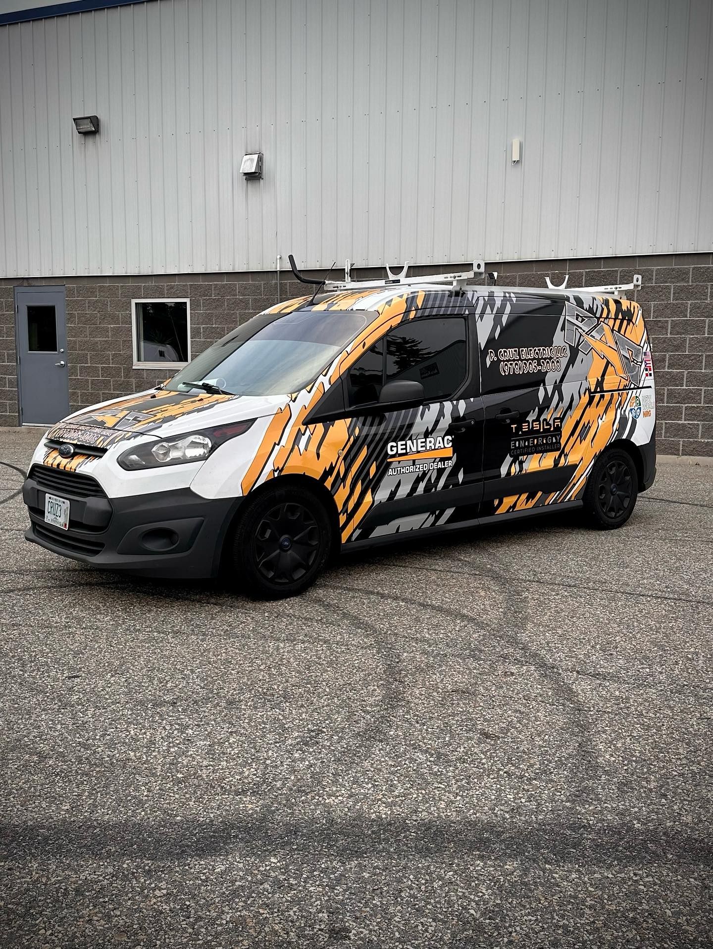 Ford Transit Connect van with orange and black abstract graphics parked in front of a gray building.