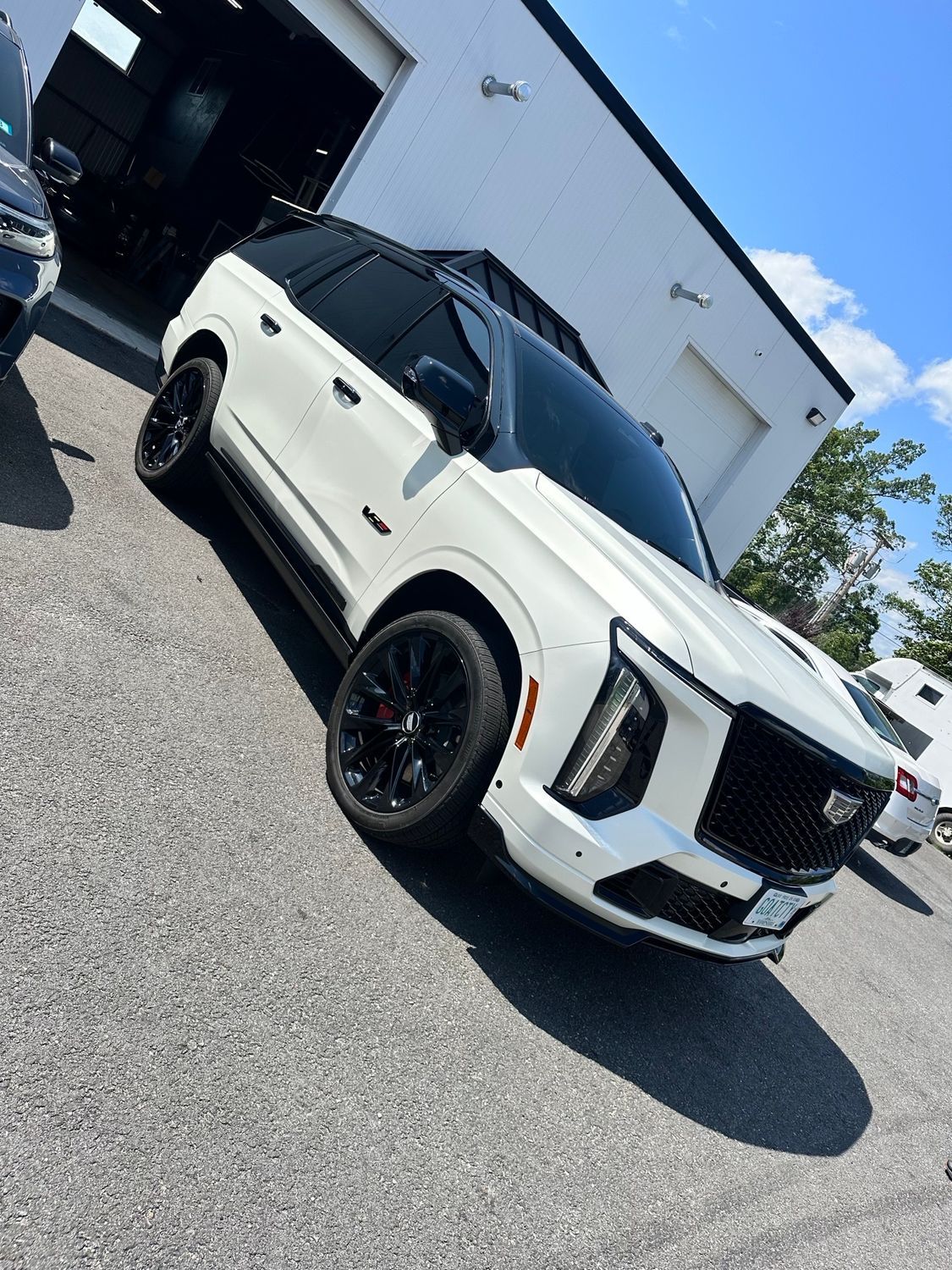 White Cadillac SUV parked on asphalt with a black roof, black wheels, and a garage in the background.