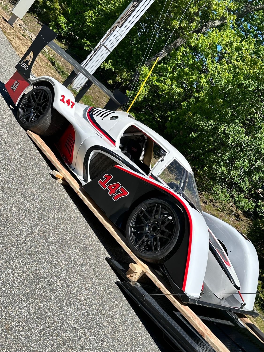 White race car with black and red accents, number 247, on wooden ramps outdoors.