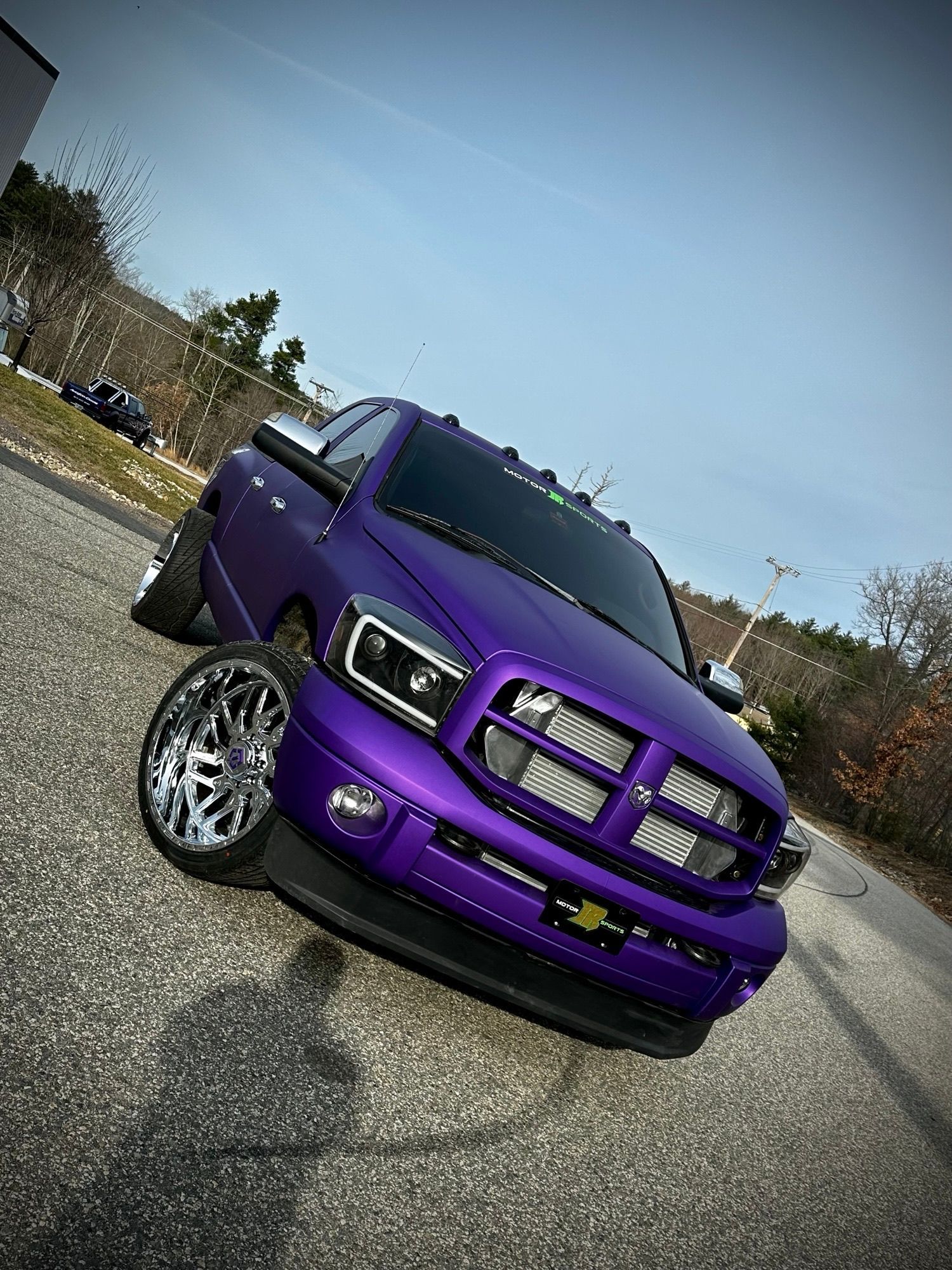 Purple Dodge Ram truck, lowered suspension, chrome wheels, on a road, sunny day.