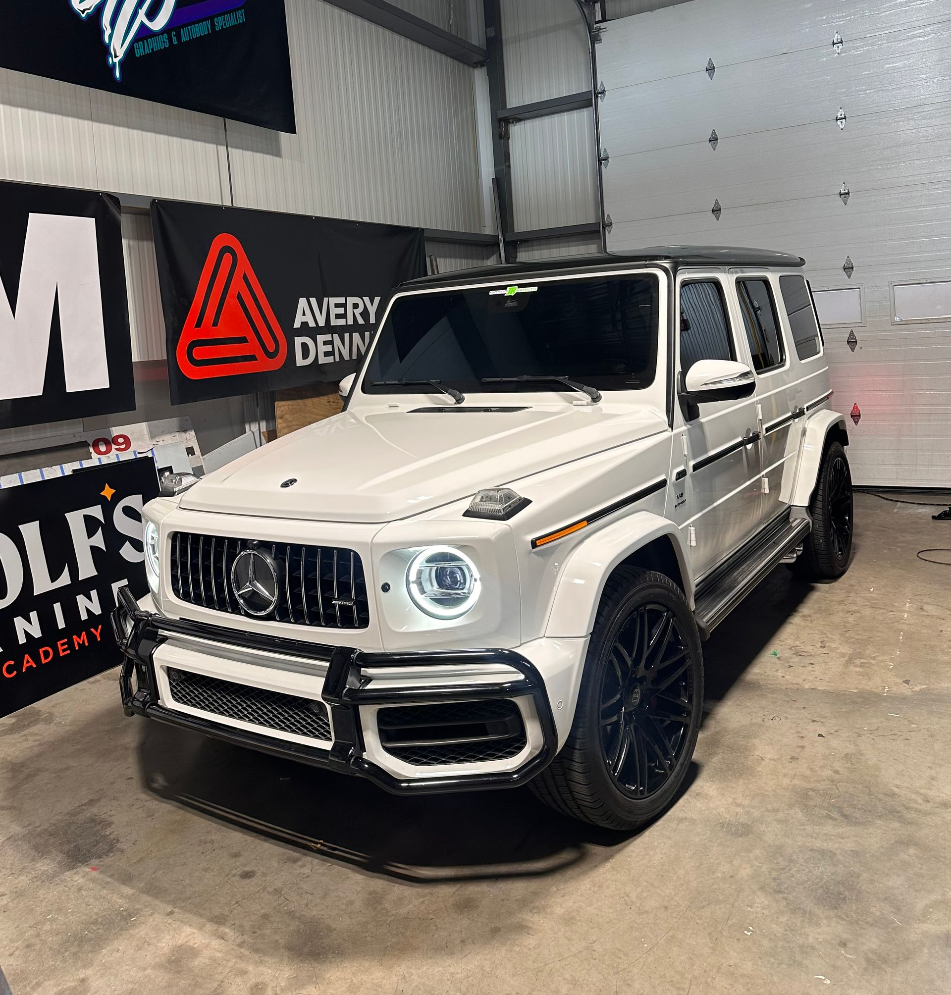 White Mercedes-Benz G-Class SUV with black accents in a garage with banners.
