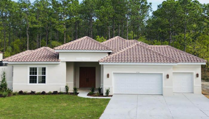 A white house with a red tile roof is surrounded by trees.