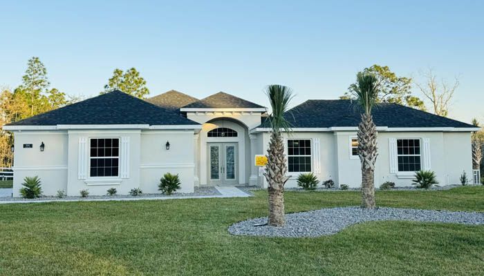 A large white house with a black roof and palm trees in front of it.