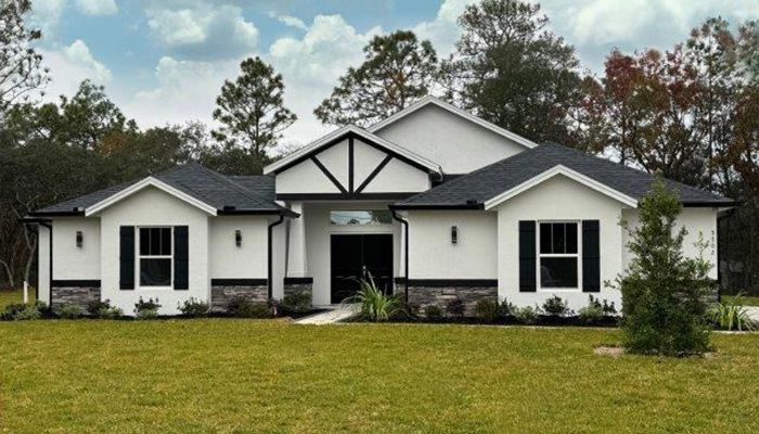 A white house with black shutters is sitting on top of a lush green field.