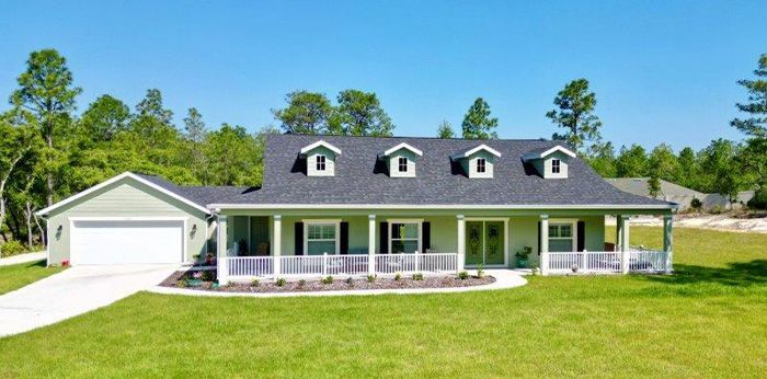 A large house with a porch and a garage in the middle of a lush green field.