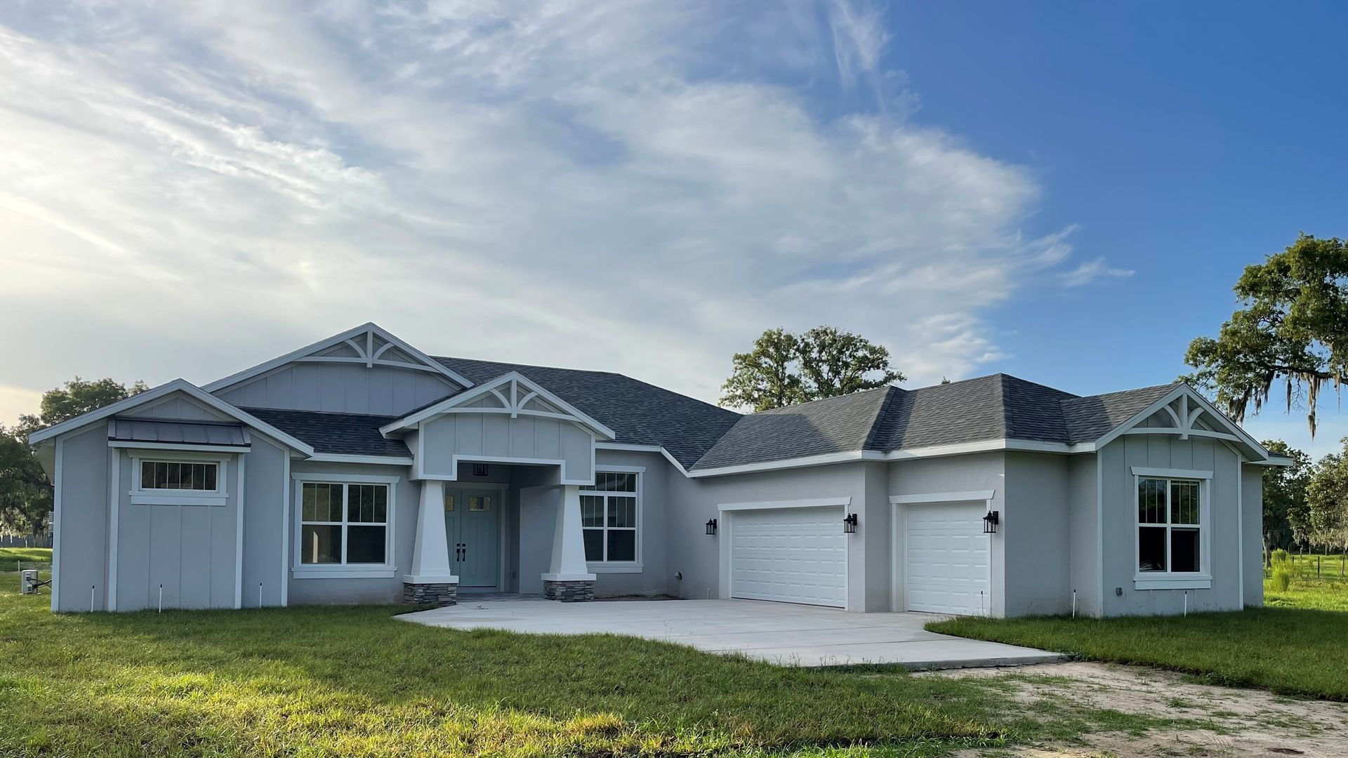 A large white house with a gray roof is sitting on top of a lush green field.