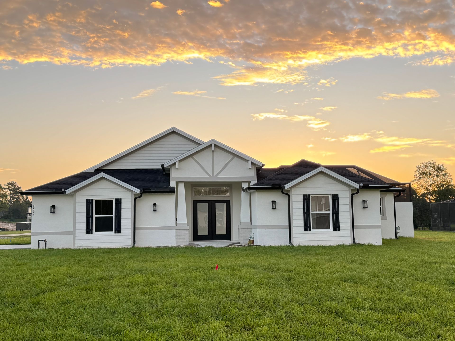 A white house with black shutters is sitting on top of a lush green field.