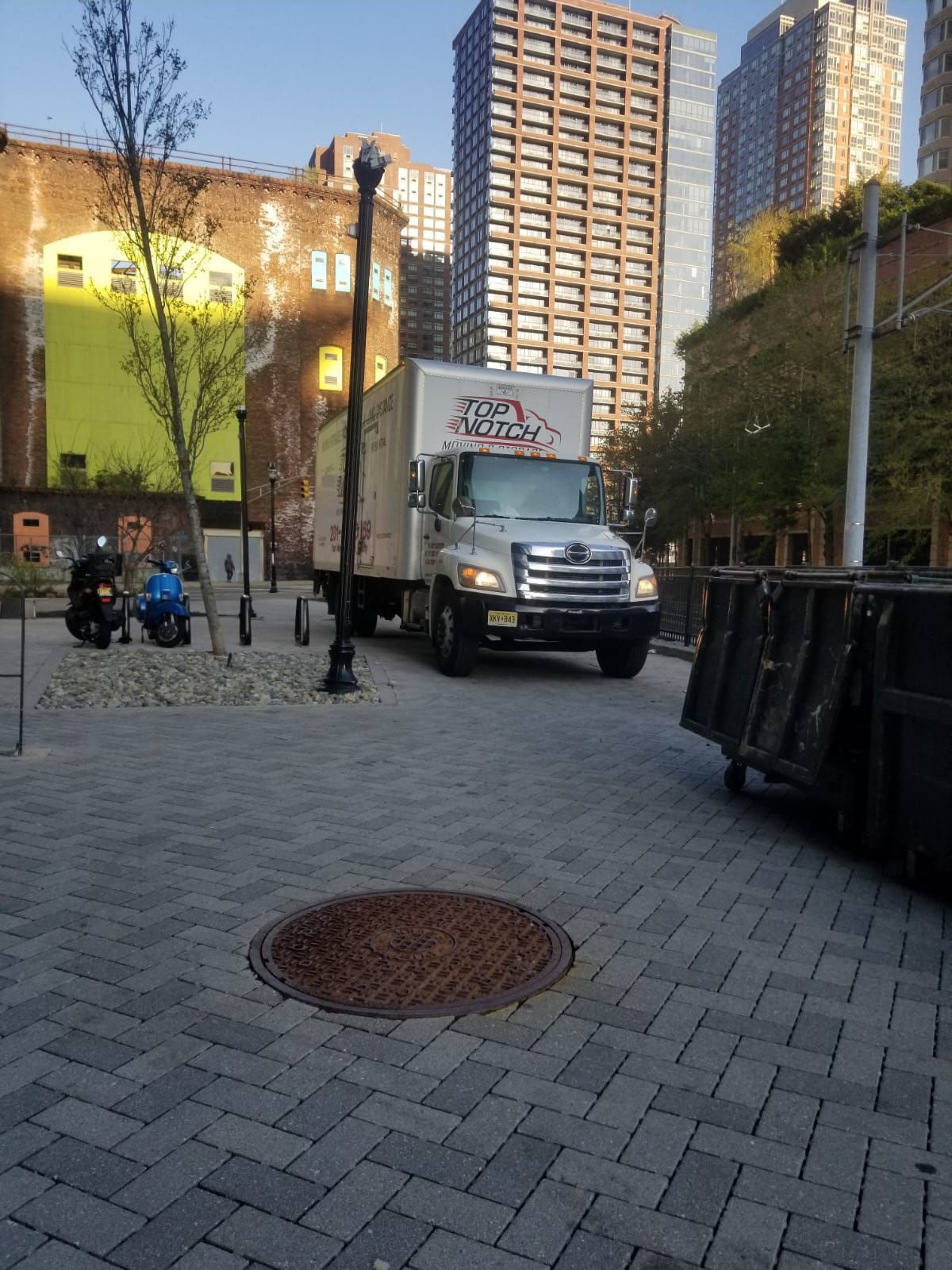 A moving truck is parked on a brick sidewalk in front of a building.