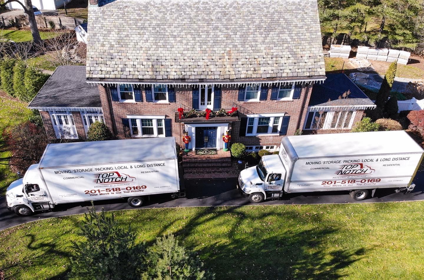 Two moving trucks are parked in front of a large brick house.