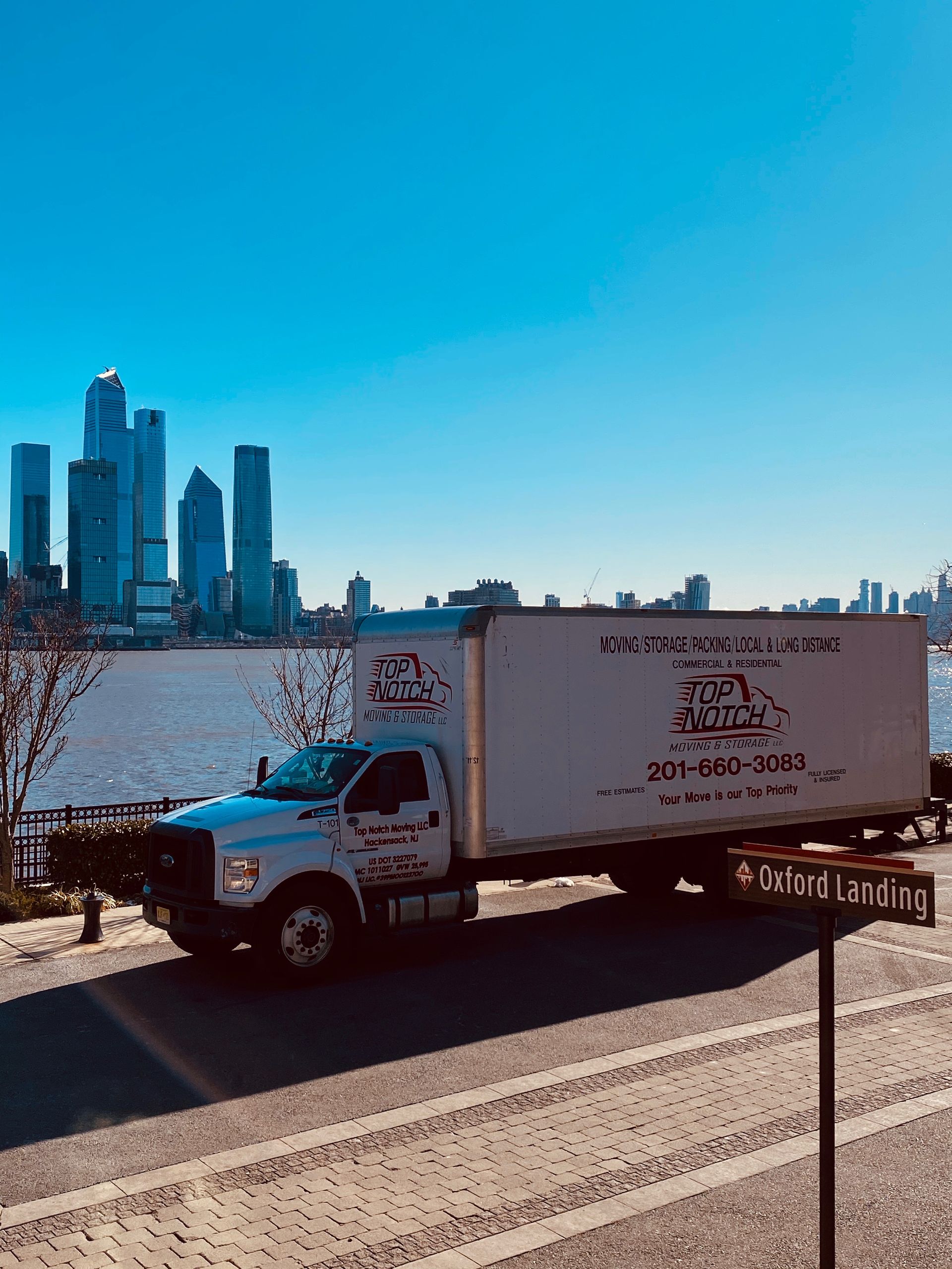 A white truck is parked on the side of the road in front of a city skyline.