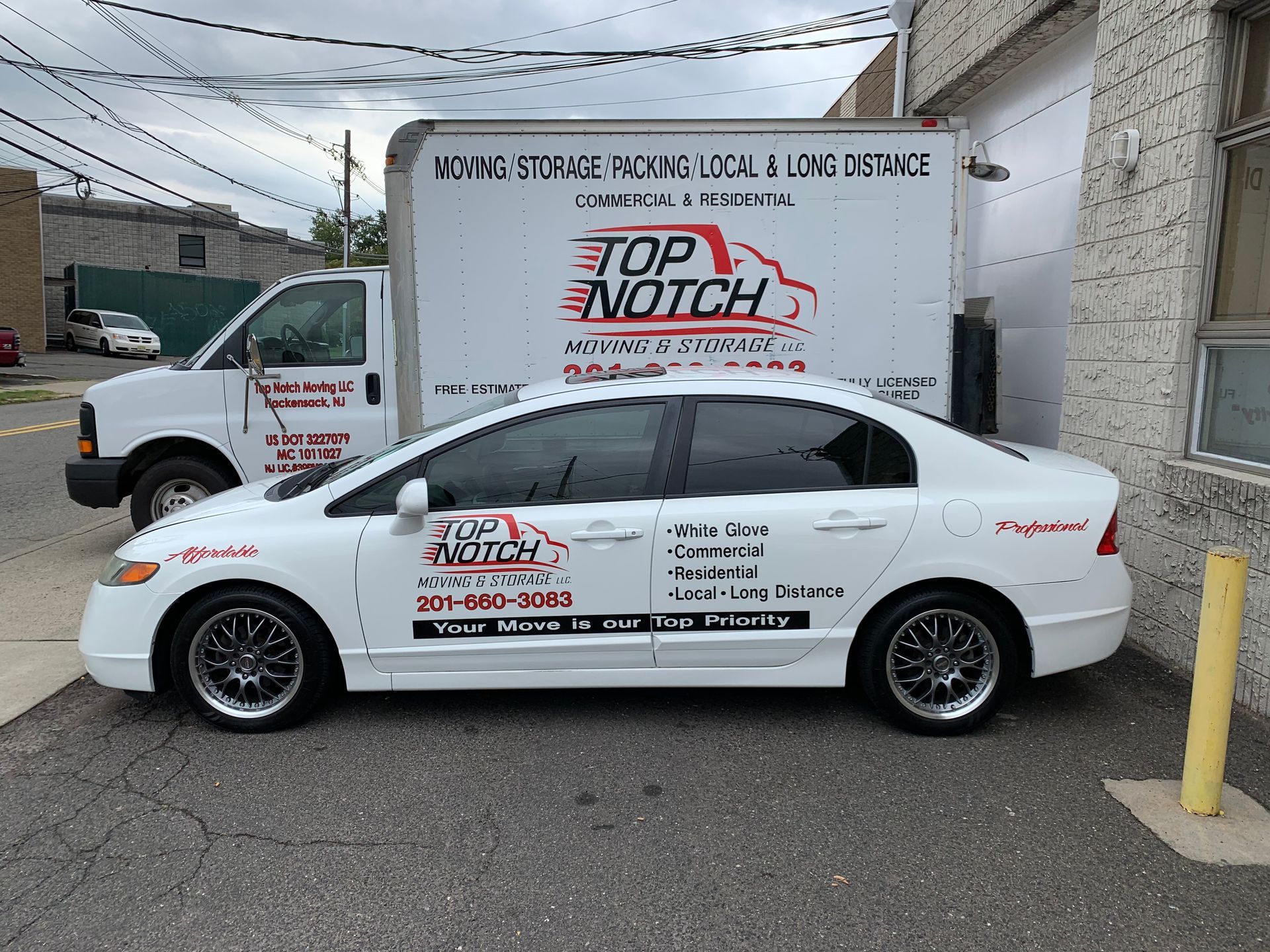 A white car is parked in front of a top notch moving truck.
