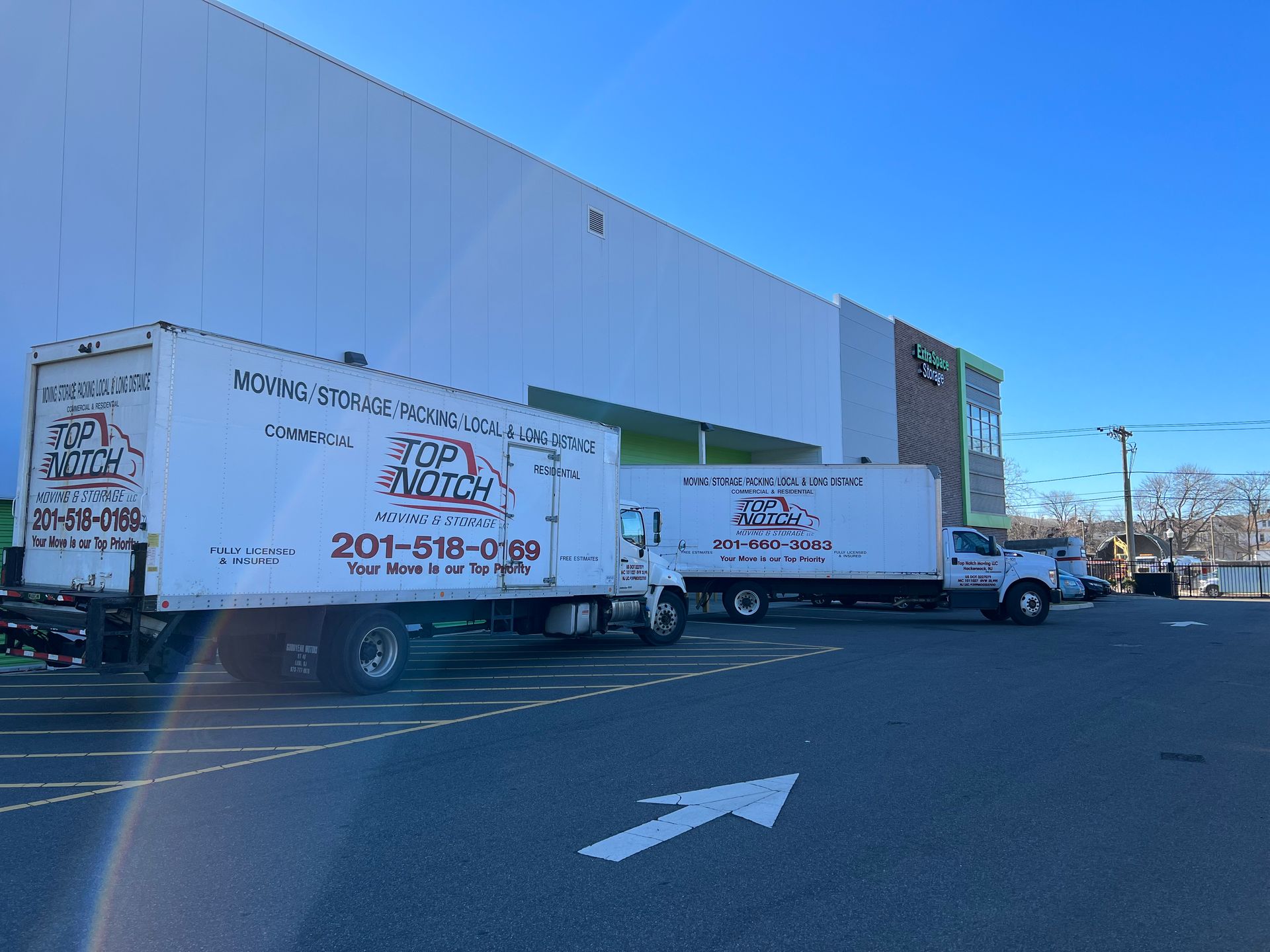 Two moving trucks are parked in a parking lot in front of a building.