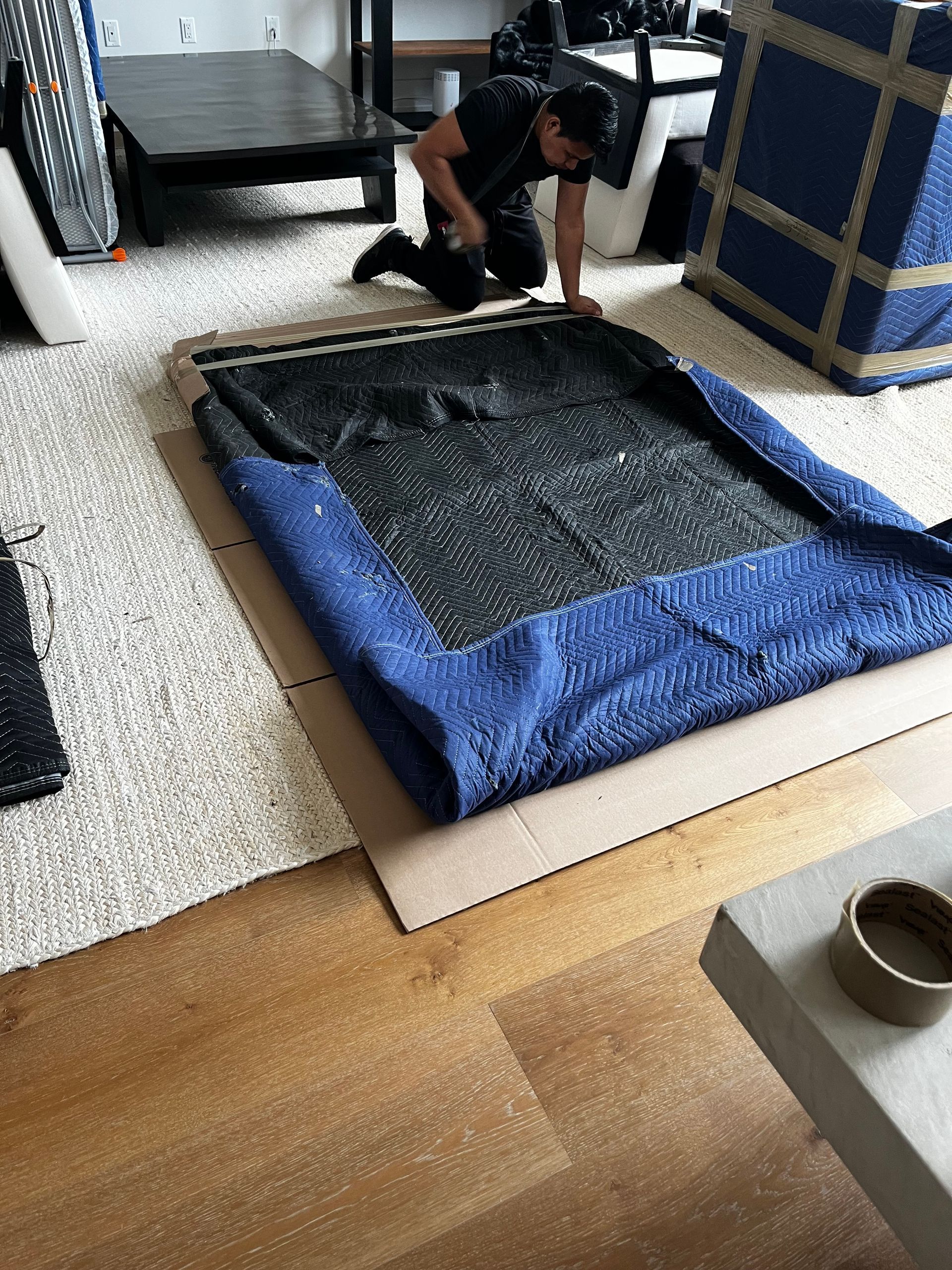 A man is kneeling on the floor next to a blue tarp.