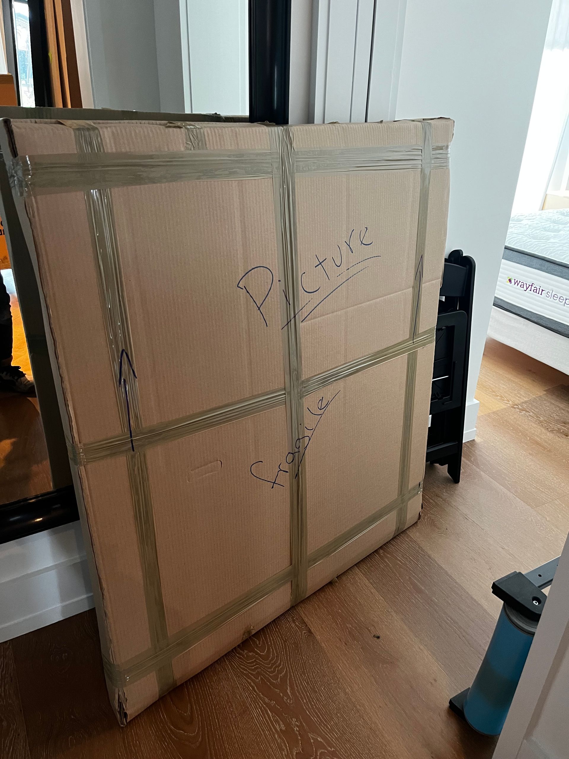 A large cardboard box is taped to the floor in a living room.