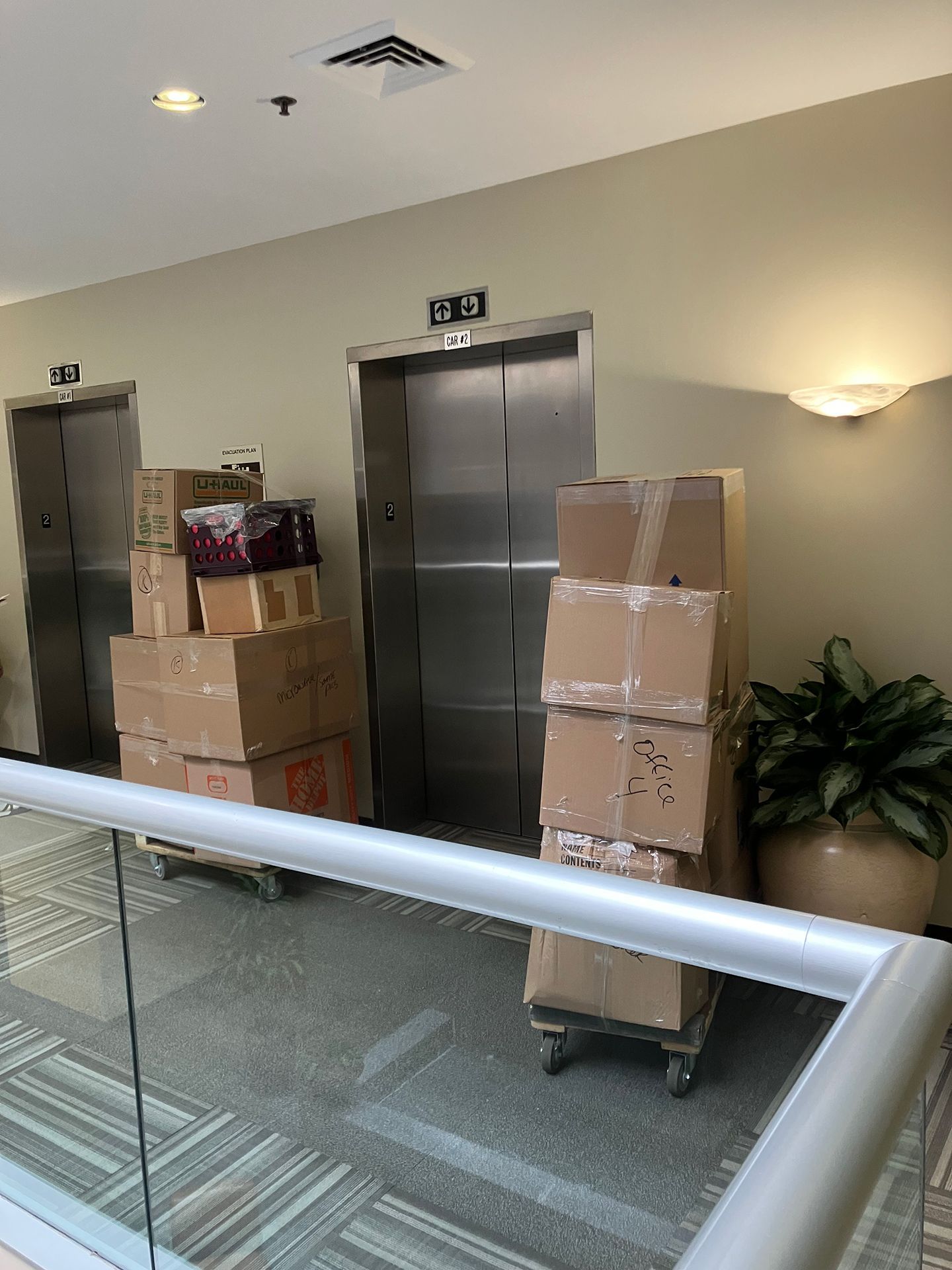 Two elevators are filled with boxes in a hallway.