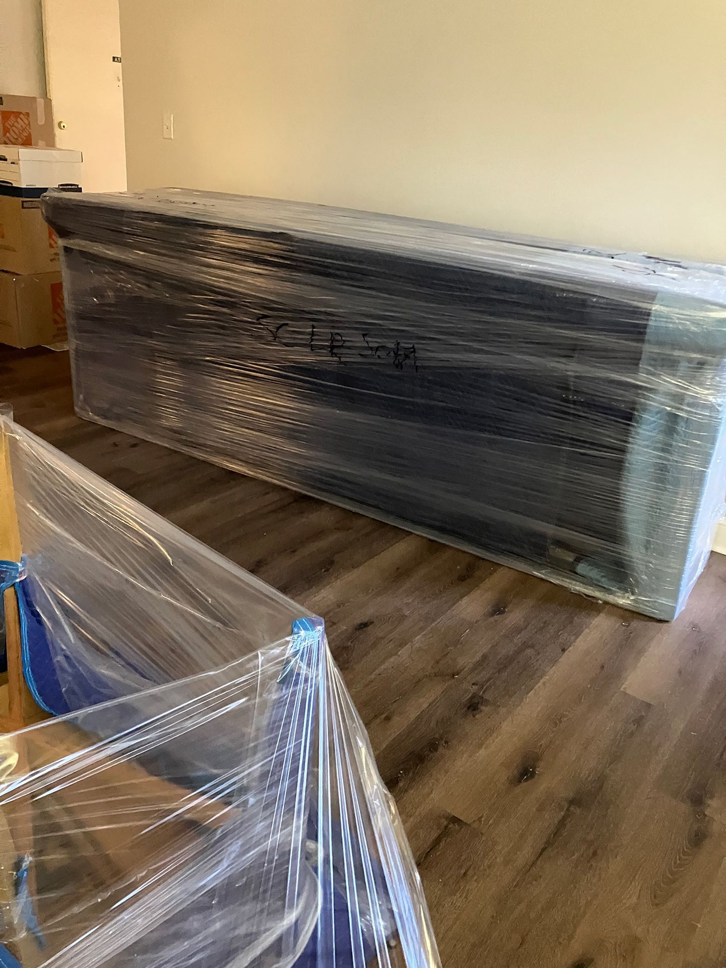 A large box wrapped in plastic is sitting on a wooden floor in a living room.