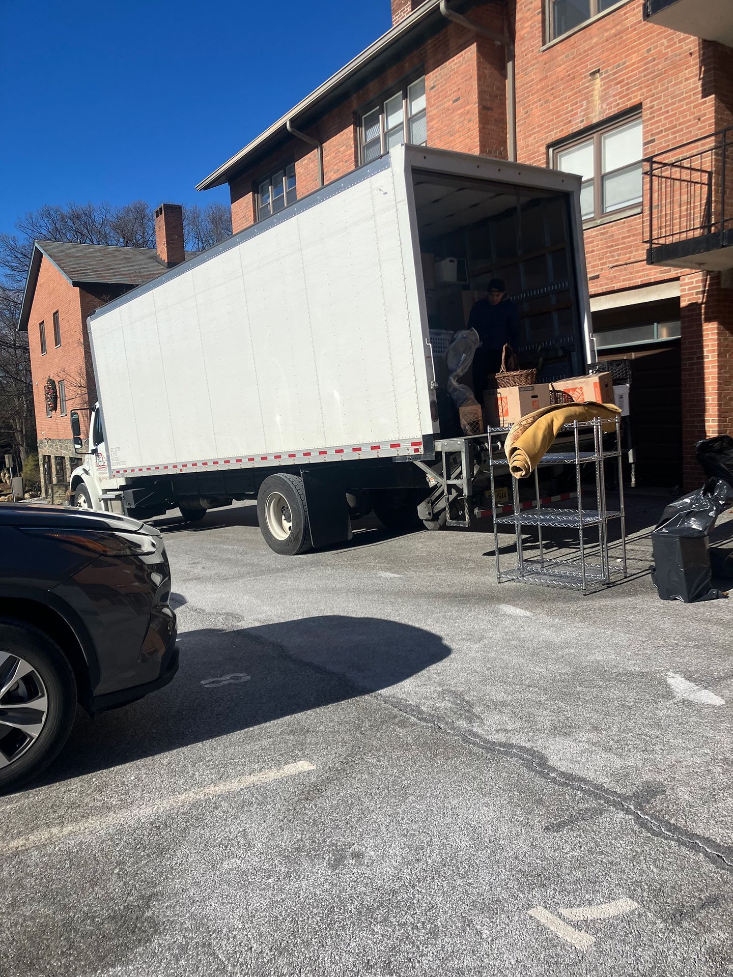 A moving truck is parked in a parking lot in front of a brick building.