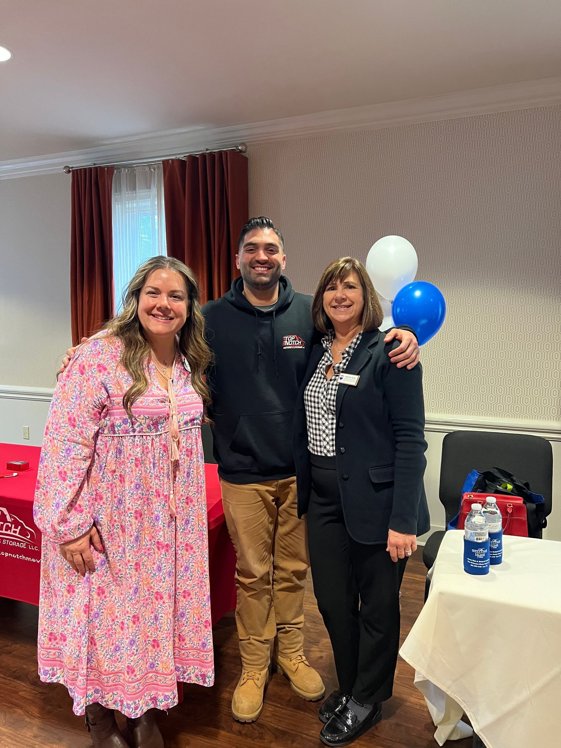 A man and two women are posing for a picture in a room with balloons.