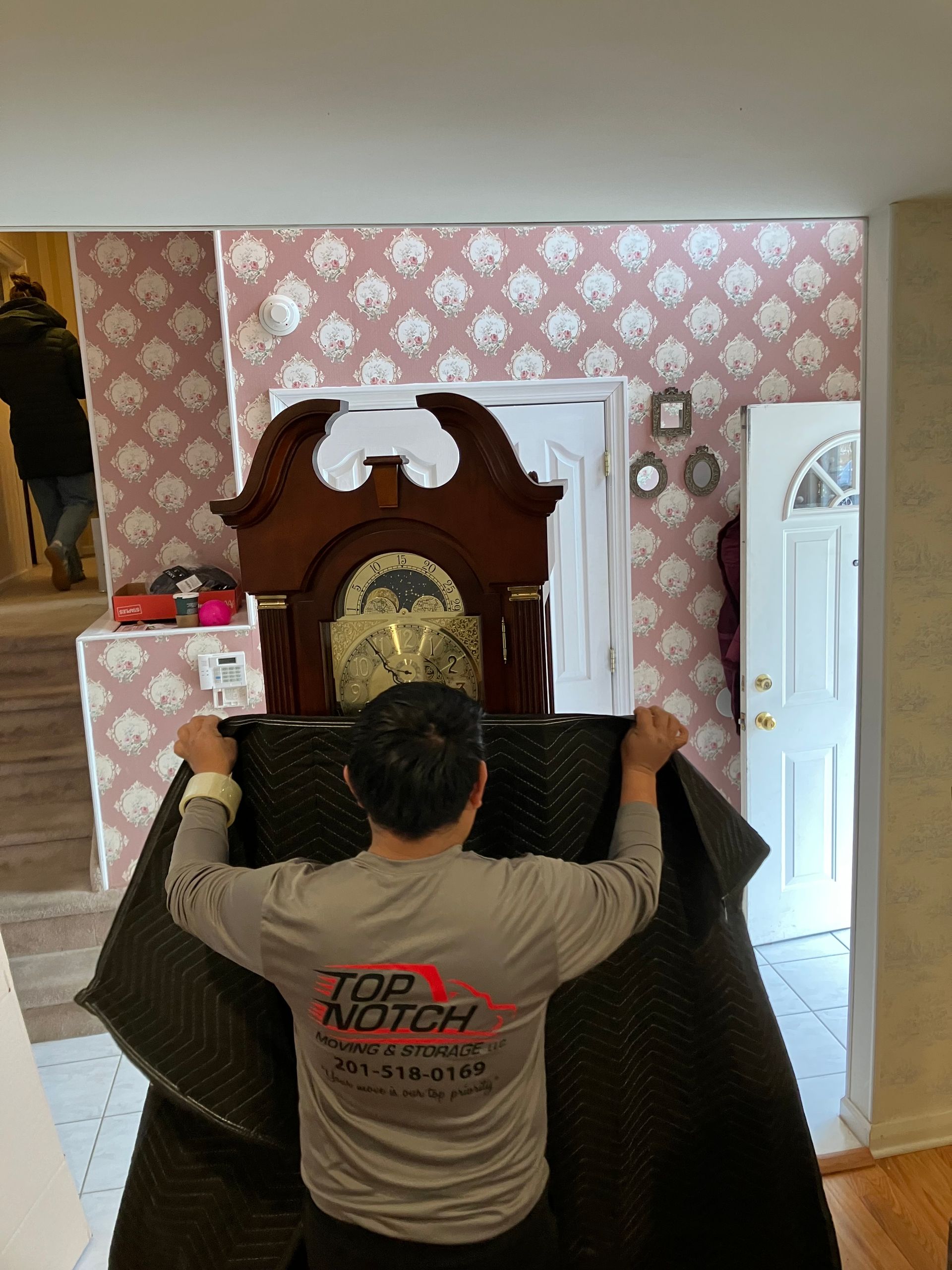 A man in a top notch shirt is moving a grandfather clock.