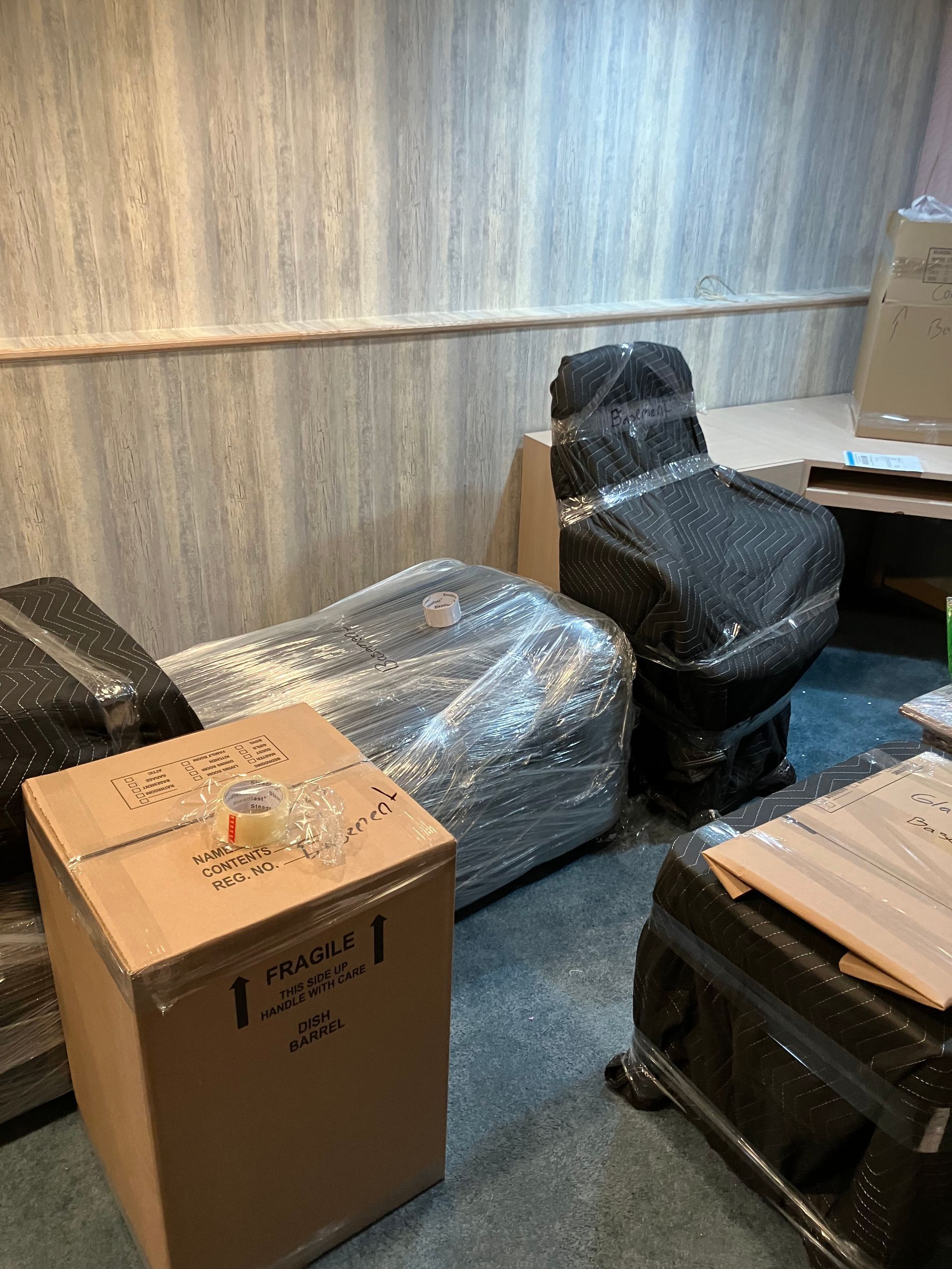 A room filled with boxes and chairs wrapped in plastic.