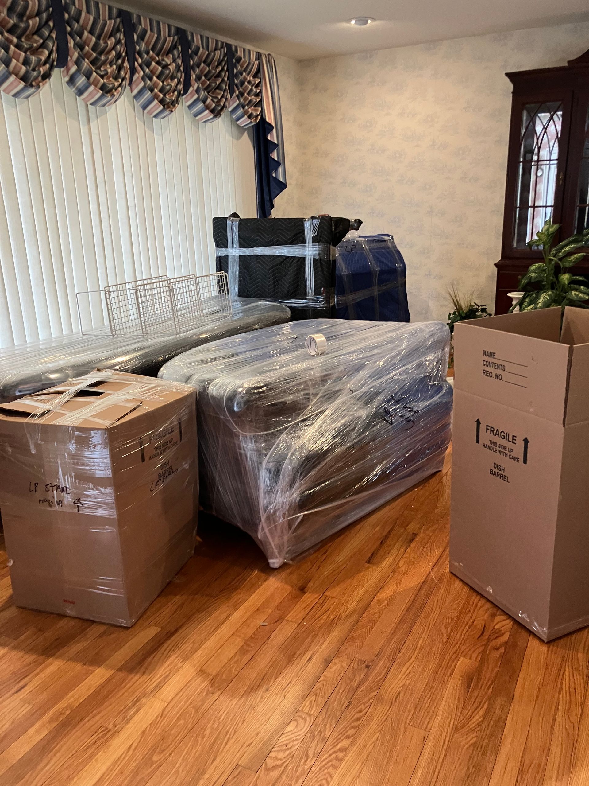A living room filled with boxes and a couch wrapped in plastic.