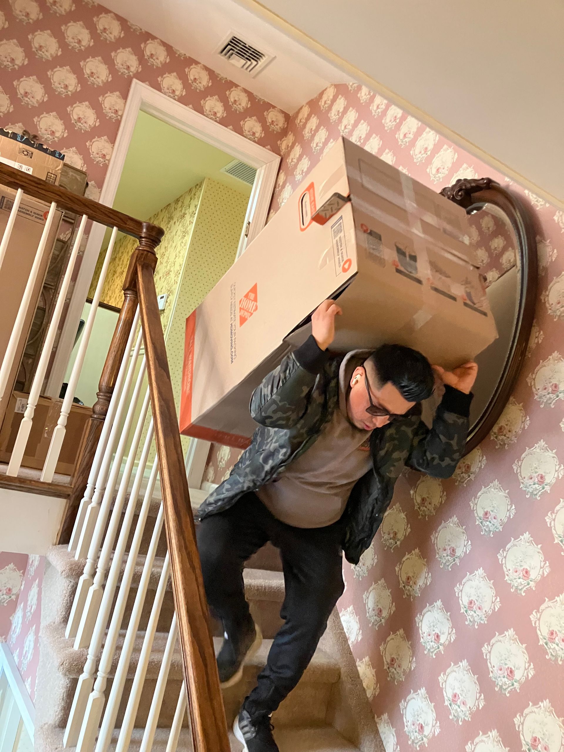A man is carrying a large cardboard box on his shoulders up a set of stairs.