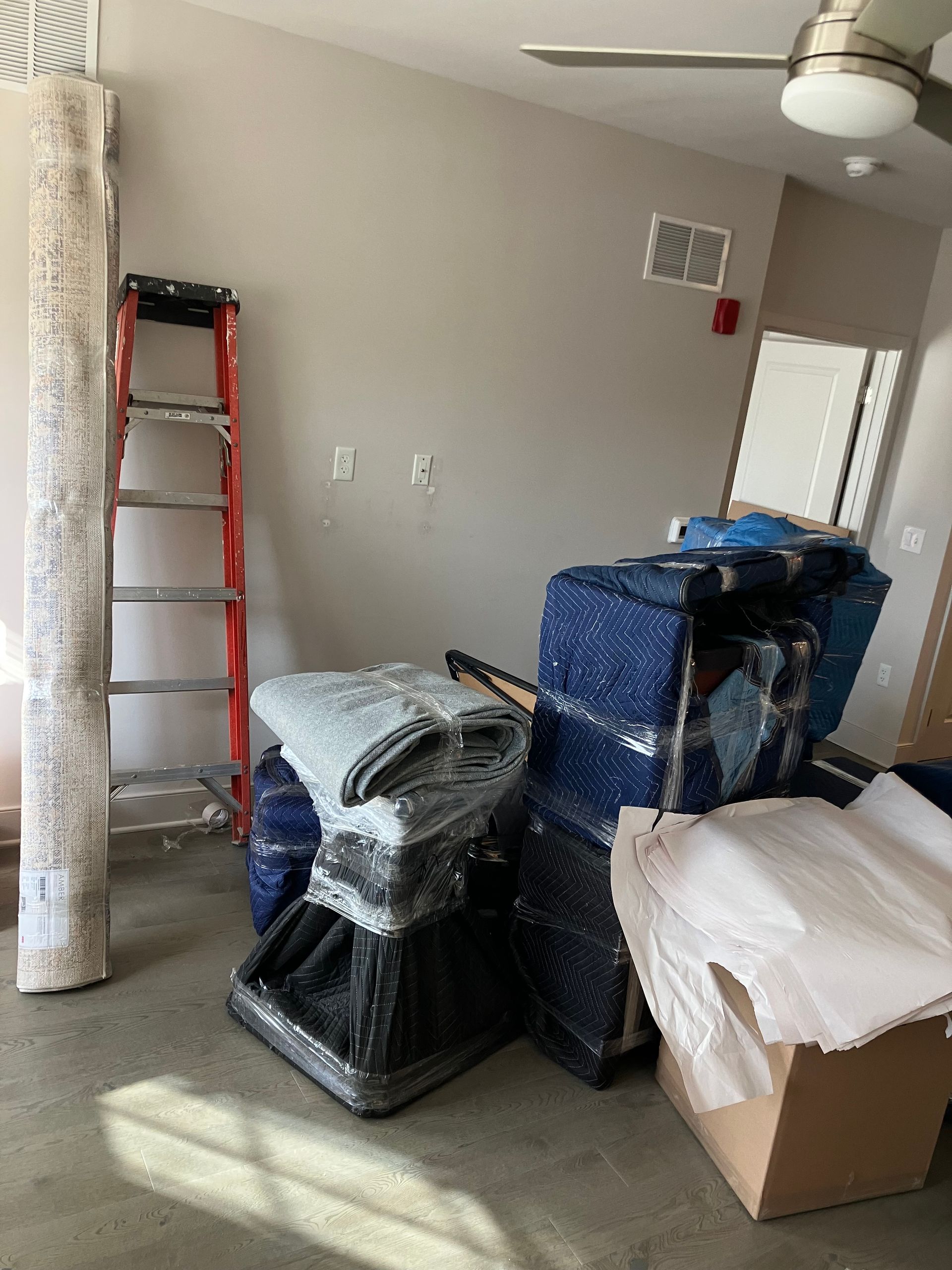 A room filled with boxes, blankets, and a ladder.