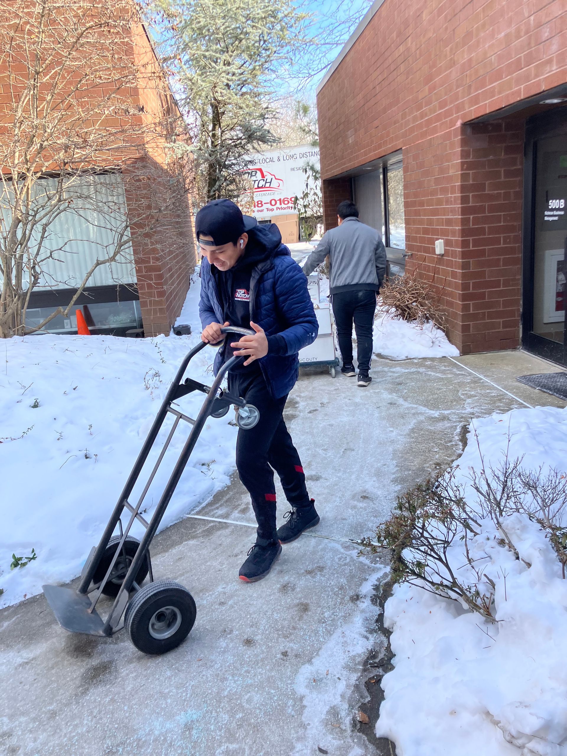 A man is pushing a hand truck down a snowy sidewalk.