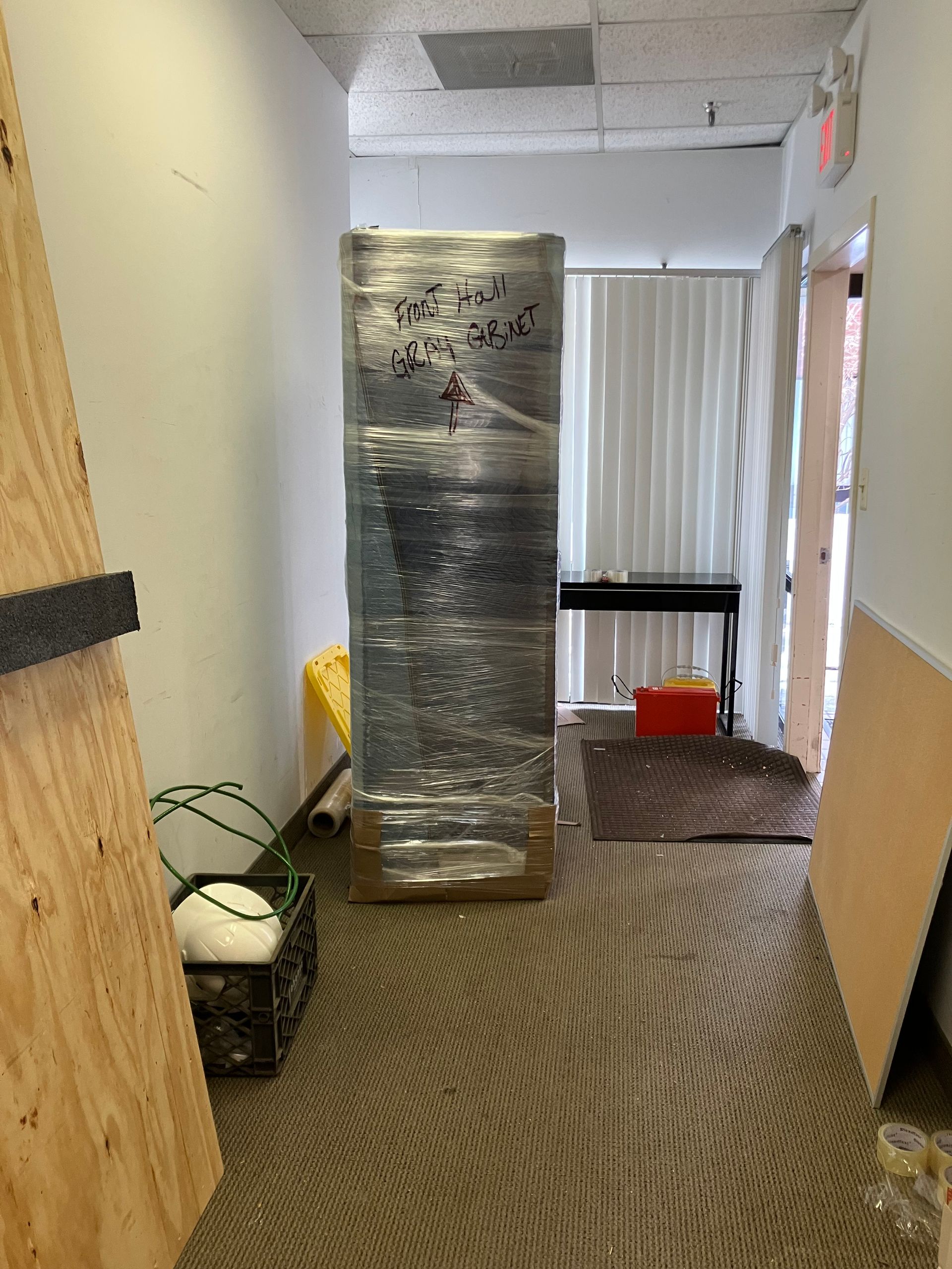 A refrigerator is wrapped in plastic in a hallway.