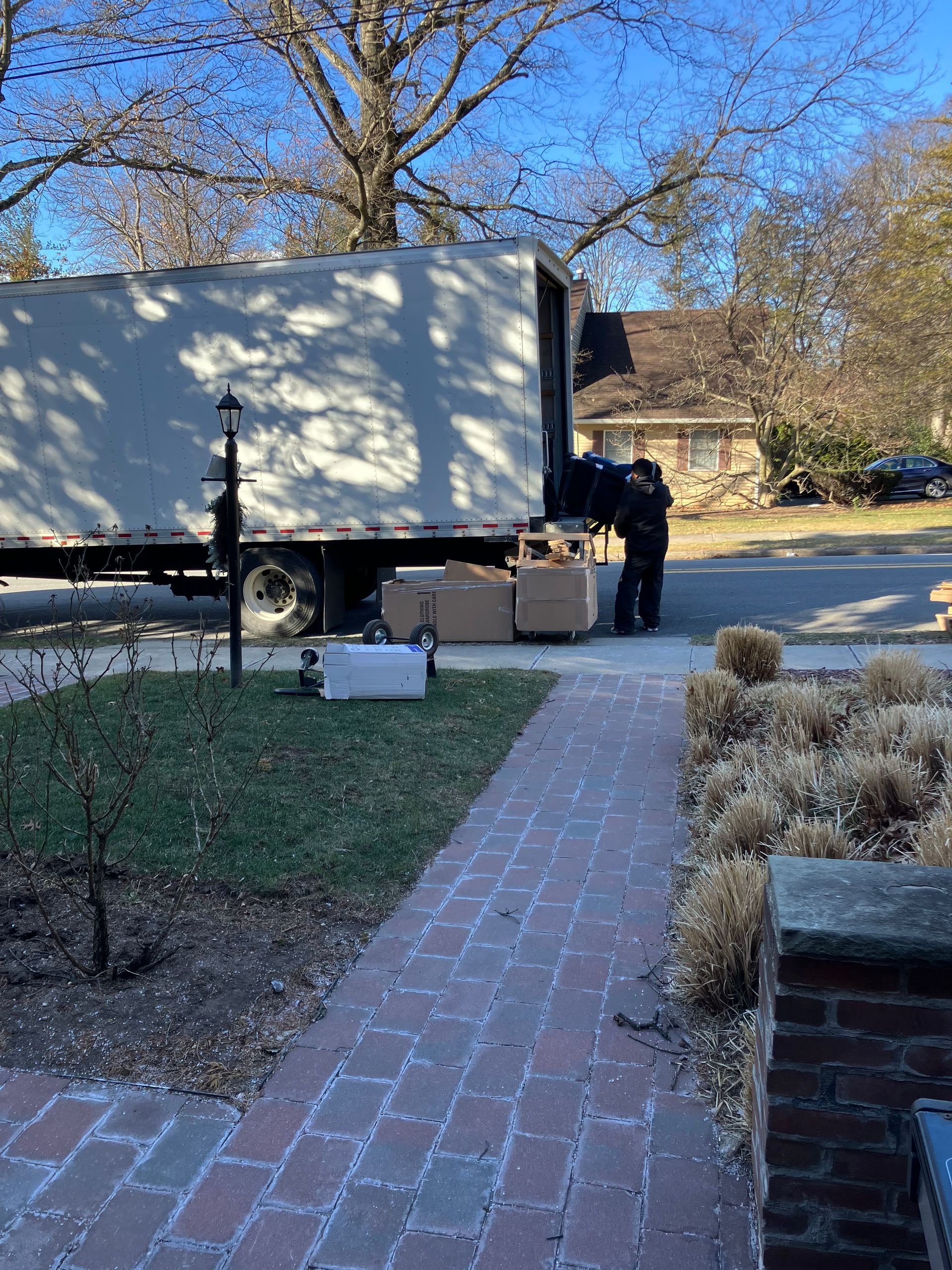A moving truck is parked on the side of the road next to a brick walkway.