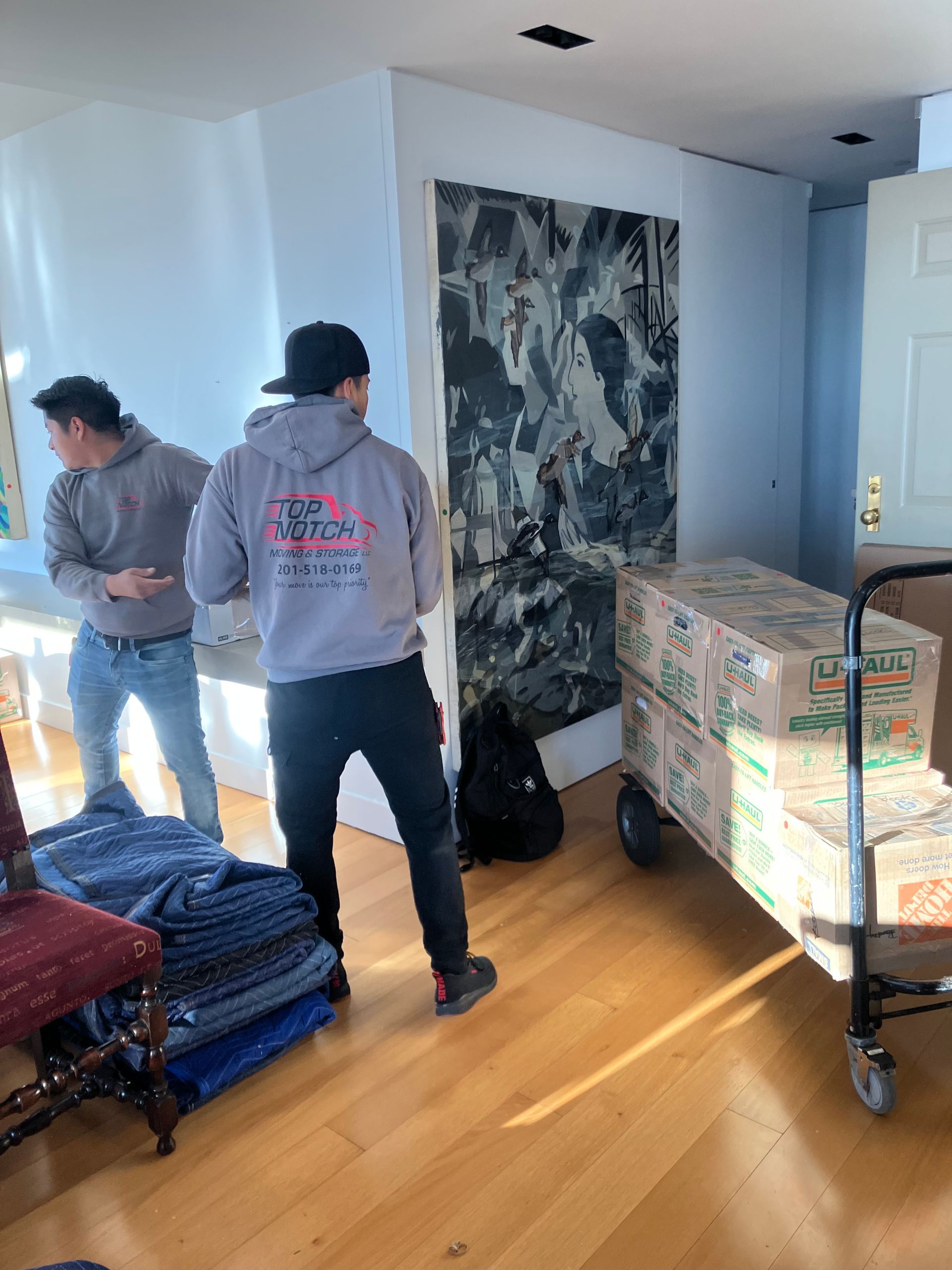 Two men are moving boxes on a cart in a living room.